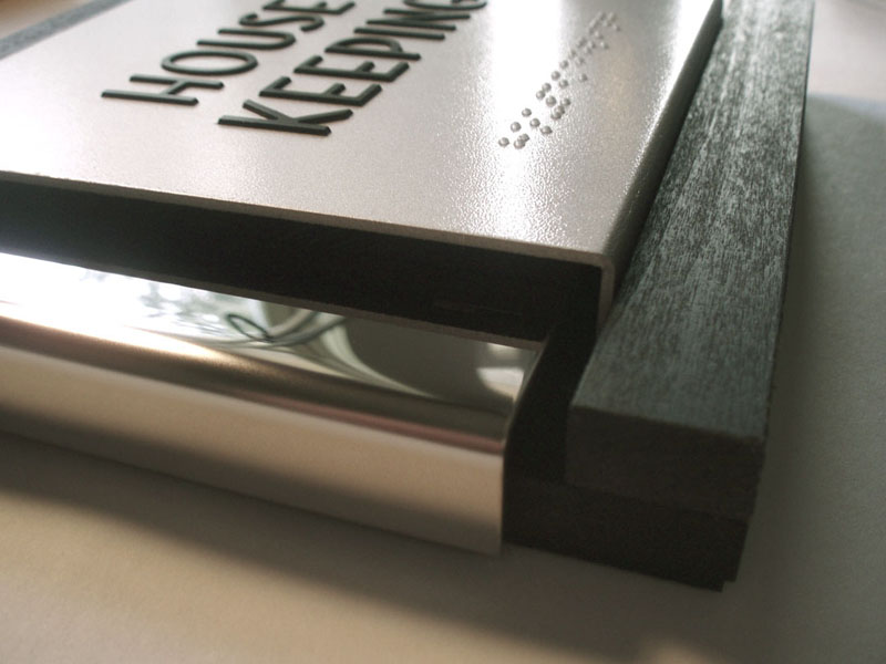 This sign program has been used on four of the Palomar hotels. The sign is an assembly of nesting shapes with returns, both wood and metal. The middle form is mirror polished stainless. The tactile plate is aluminum with applied copy and braille. The back plate is painted / stained wood.